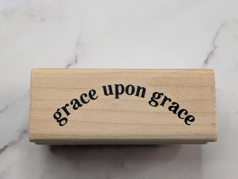 A rubber stamp mounted on a wooden block that says, "grace upon grace."