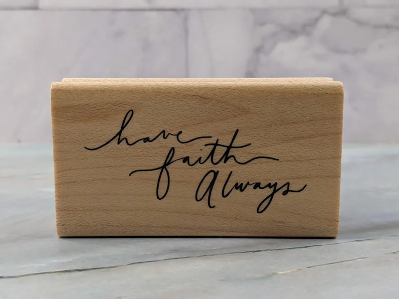 A rubber stamp mounted on a wooden block that says, "Have faith always."