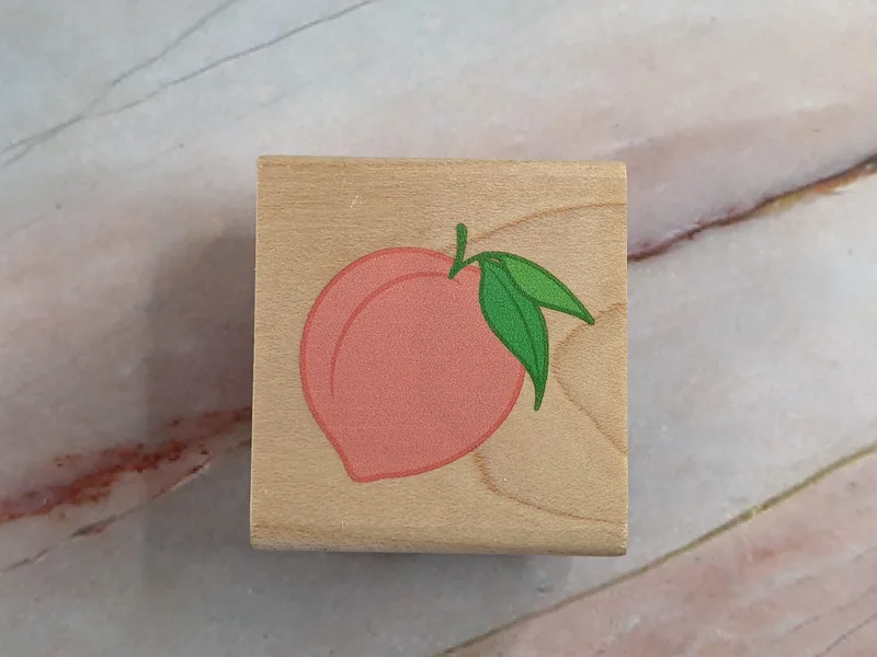 A rubber stamp with an image of a peach, mounted on a wooden block.