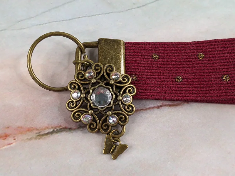 A burgundy corduroy wristlet keychain with antique-gold hardware with rhinestones and a butterfly charm.