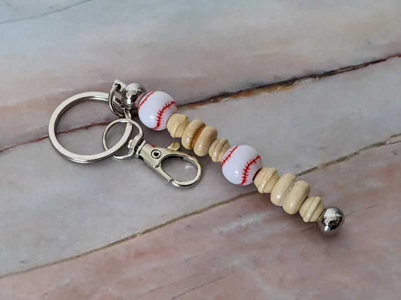 A bag charm with baseball beads and natural wooden beads that includes a silver metal keyring.