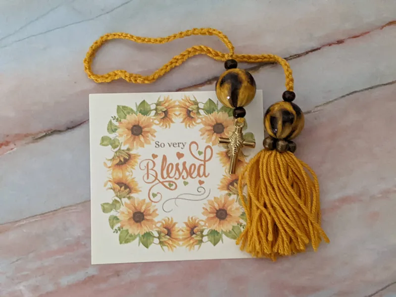 A yellow yarn bookmark with a tassel and a cross pendant, along with two beads that have a leopard print design.