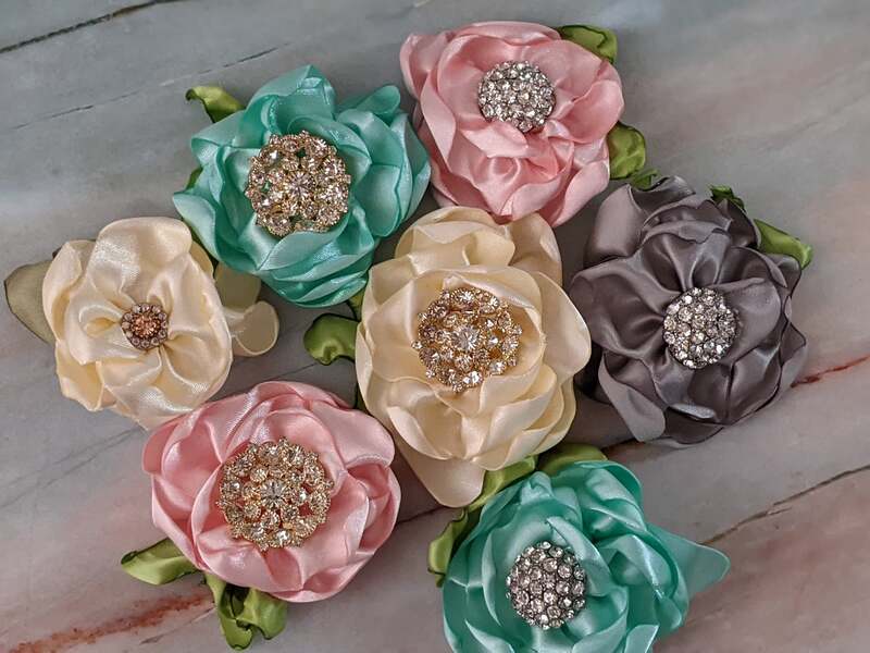 An assortment of handmade satin flowers in various colors with gorgeous rhinestone accents to attach to wrapped gifts.