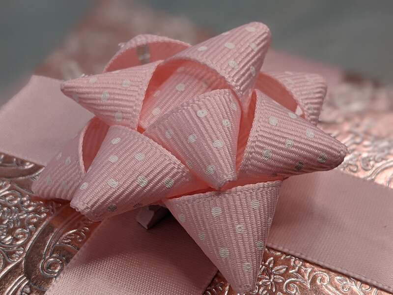 A gift bow clip that attaches on a gift, handmade with pink grosgrain ribbon with small white polka dots.