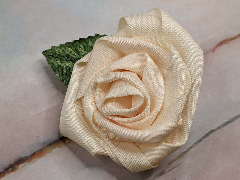 A cream-colored handmade fabric flower rosette that clips onto a wrapped gift.