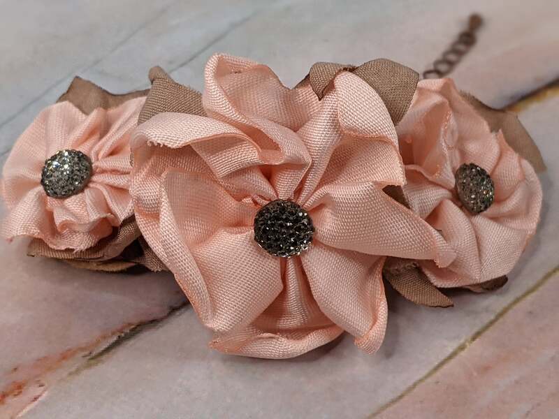 A dark gold chain bracelet with three pink fabric handmade flowers with taupe fabric leaves.