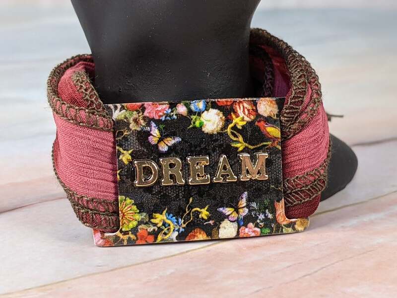 This gorgeous rosy pink cloth wrap bracelet, with a black "dream" tag with a floral design, wraps around the wrist.