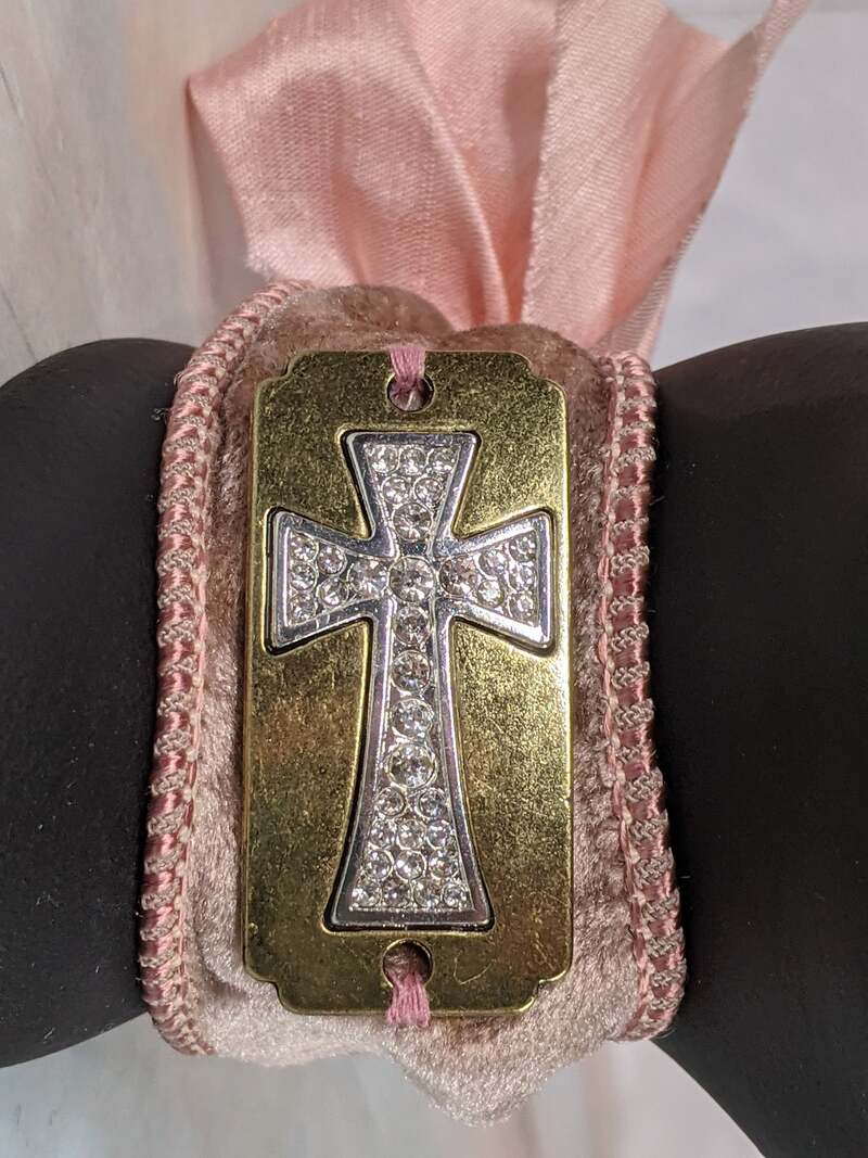 A rose velvet cuff bracelet with a pink silk ribbon bow and a gold metal cross tag.